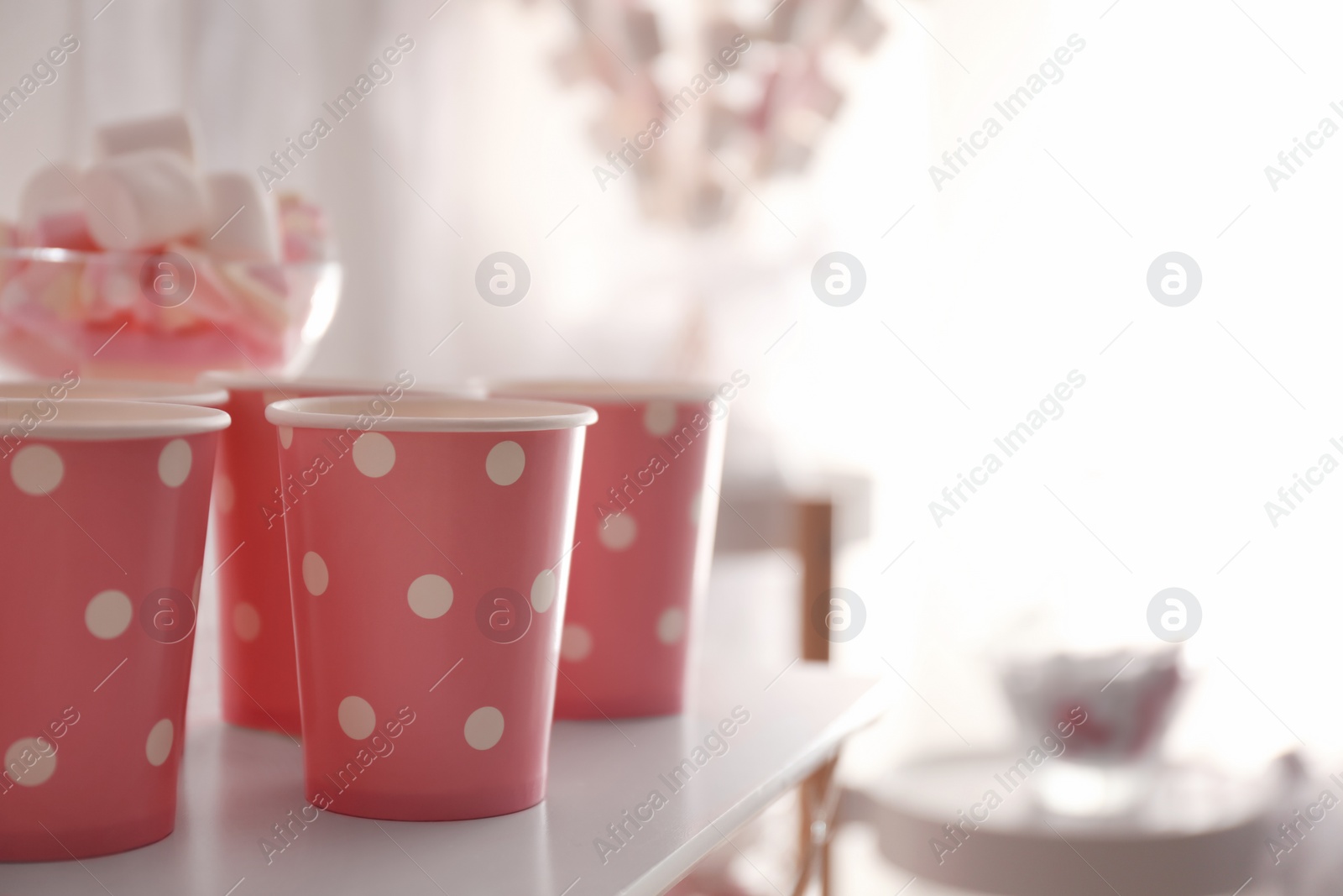Photo of Pink paper cups on white table at birthday party, closeup. Space for text