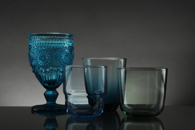 Photo of Set of different colorful empty glasses on table against grey background