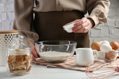 Woman adding baking powder into bowl at white wooden table, closeup