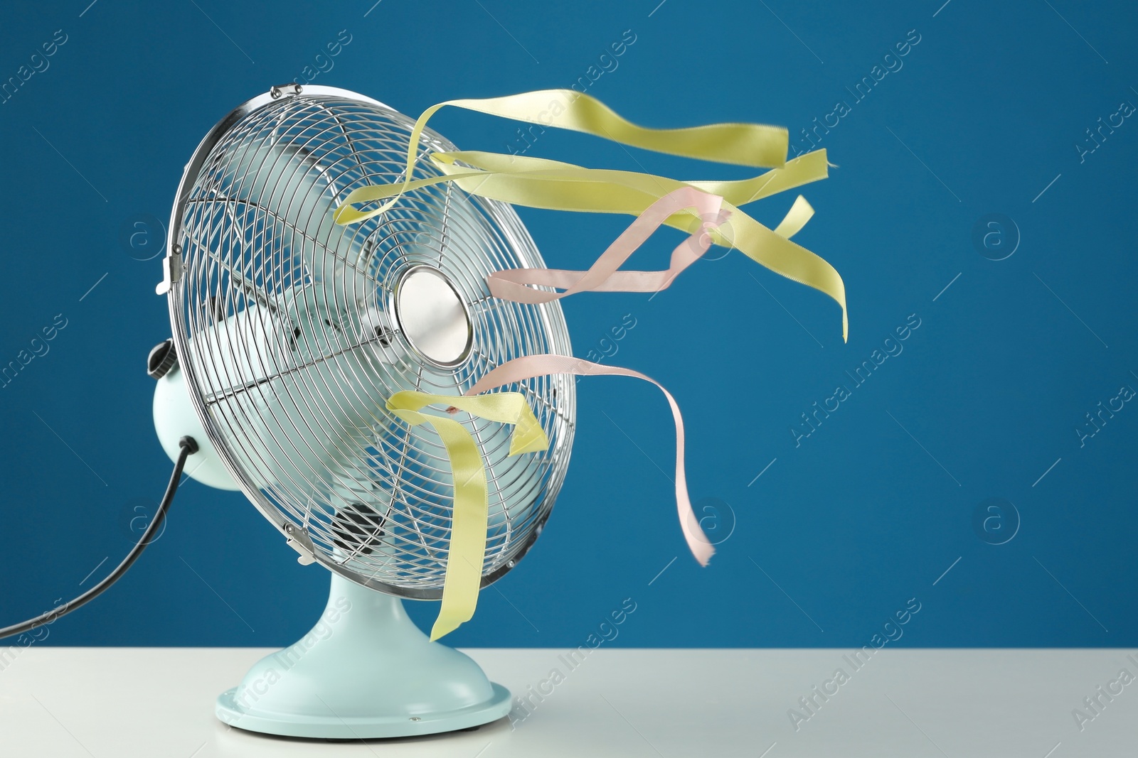 Photo of Electric fan on white table against blue background. Summer heat