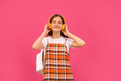 Photo of Teenage student with backpack and headphones listening to music on pink background