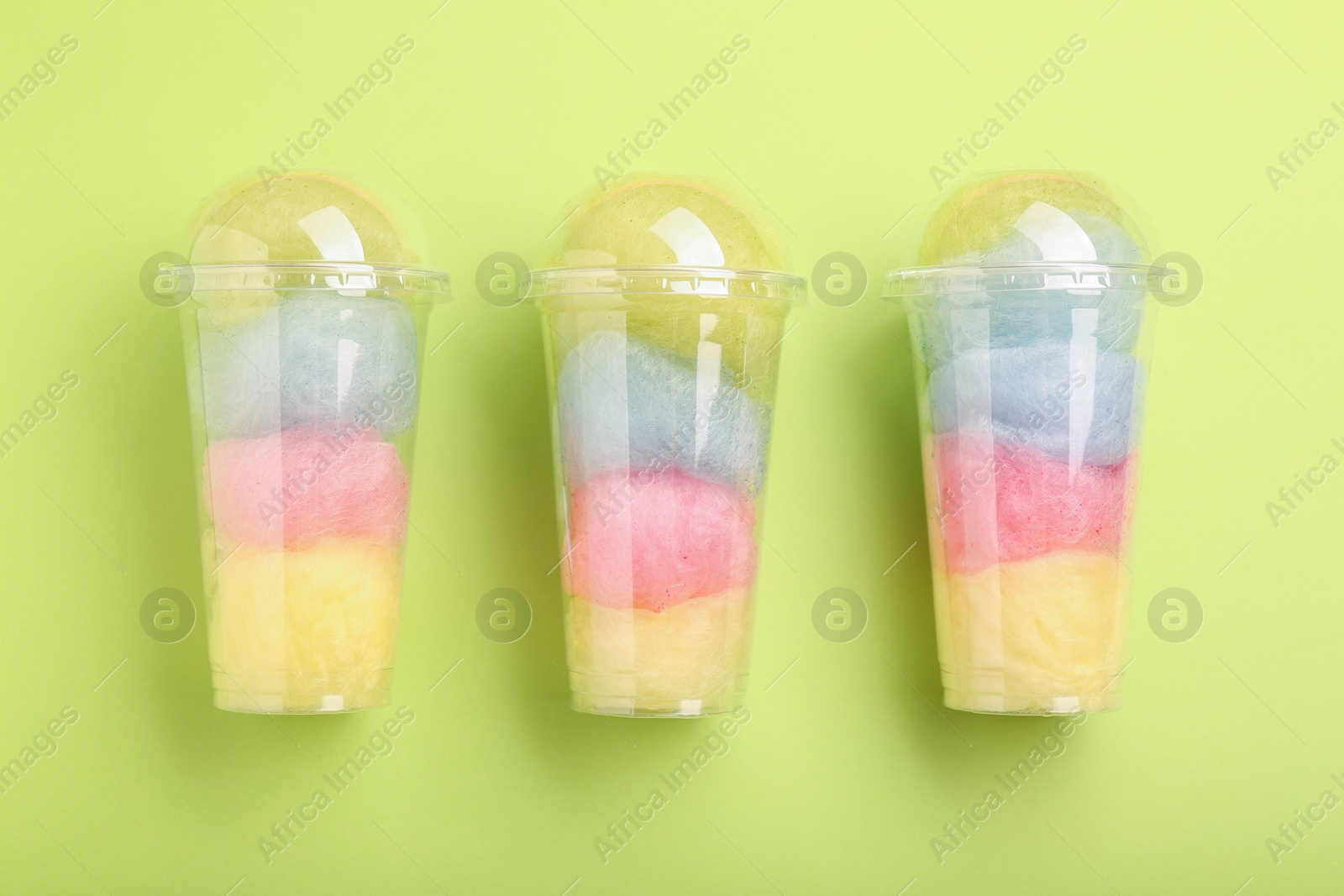 Photo of Colorful cotton candies in plastic cups on light green background, flat lay