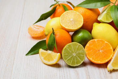 Photo of Different citrus fruits with fresh leaves on white wooden table. Space for text