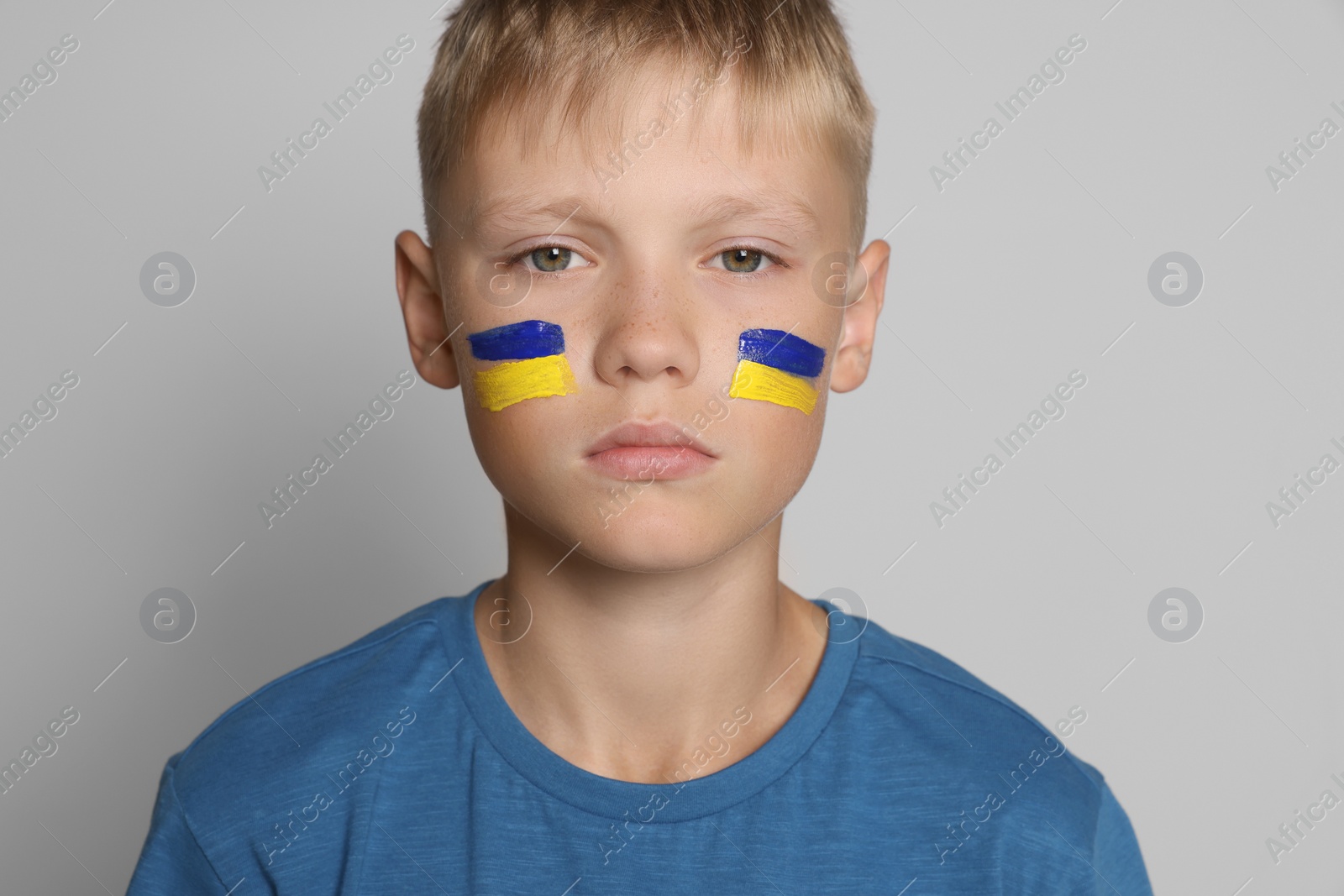 Photo of Little boy with drawing of Ukrainian flag on face against light grey background