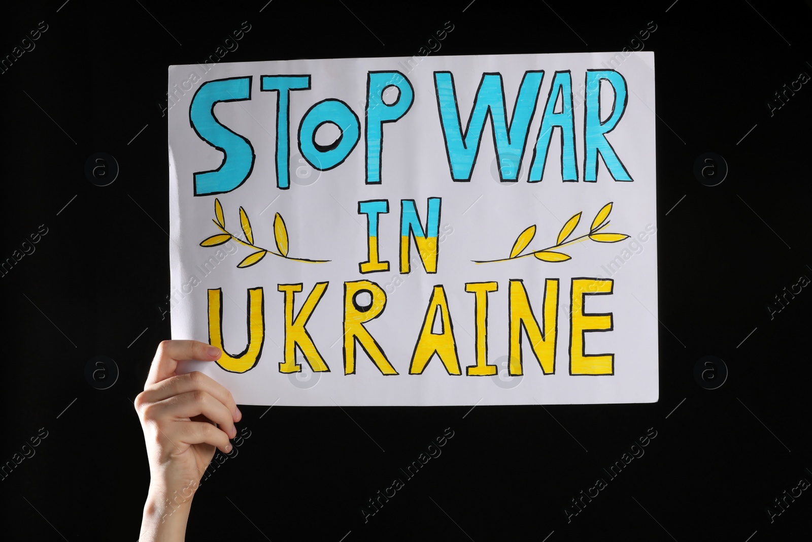 Photo of Teenage boy holding poster Stop War in Ukraine against black background, closeup
