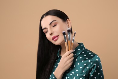 Beautiful woman with different makeup brushes on light brown background