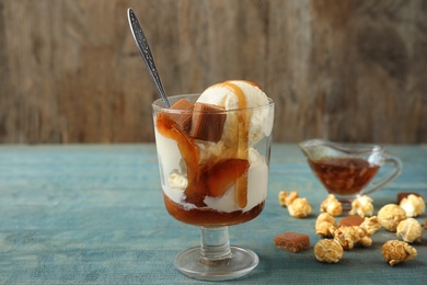 Delicious ice cream with caramel topping in dessert bowl on blue wooden table