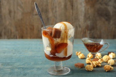 Photo of Delicious ice cream with caramel topping in dessert bowl on blue wooden table