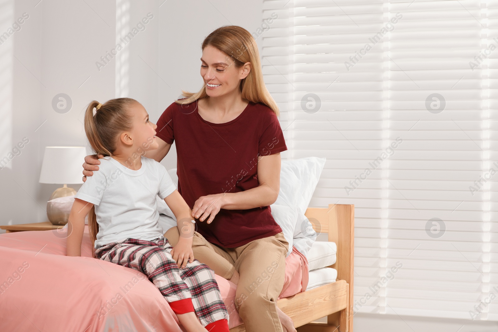 Photo of Mother applying ointment onto her daughter's arm on bed at home