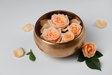Photo of Tibetan singing bowl with water and beautiful rose flowers on white background