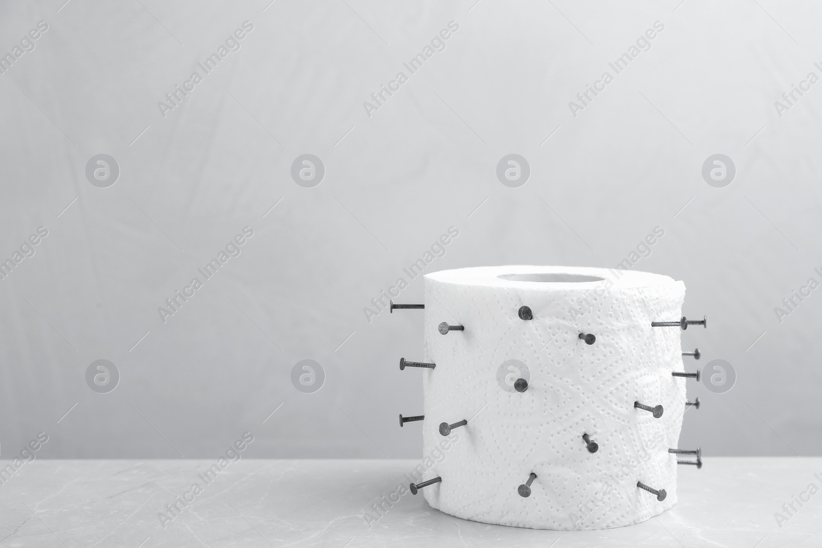 Photo of Roll of toilet paper with nails on grey marble table, space for text. Hemorrhoid problems
