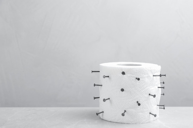 Photo of Roll of toilet paper with nails on grey marble table, space for text. Hemorrhoid problems