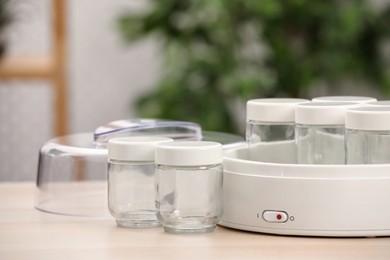 Modern yogurt maker with empty jars on table indoors. Space for text