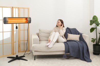 Photo of Woman warming near electric infrared heater indoors