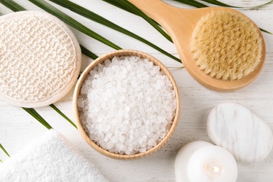 Photo of White sea salt and supplies for spa scrubbing procedure on wooden table, flat lay