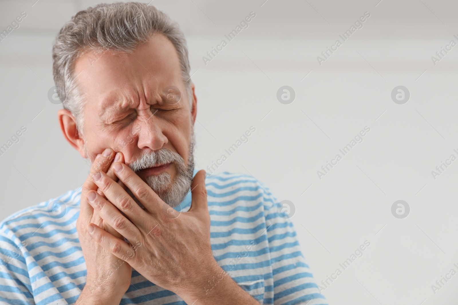 Photo of Mature man suffering from strong tooth pain on light background, space for text