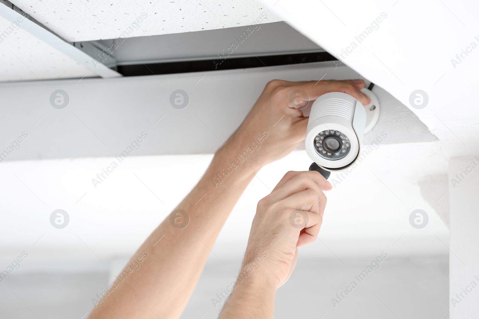 Photo of Technician installing CCTV camera on ceiling indoors, closeup