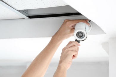 Technician installing CCTV camera on ceiling indoors, closeup