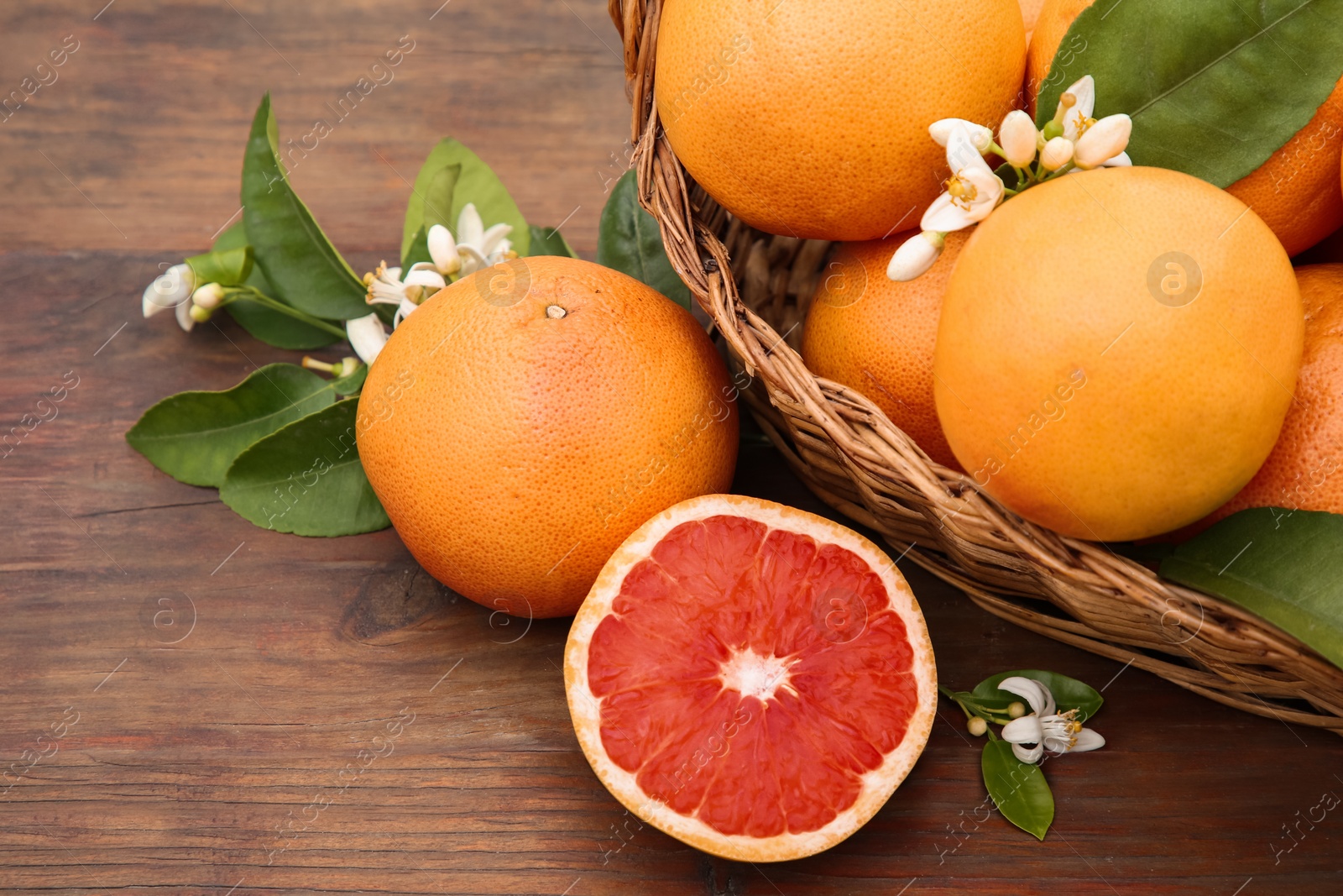 Photo of Wicker basket with fresh grapefruits and green leaves on wooden table