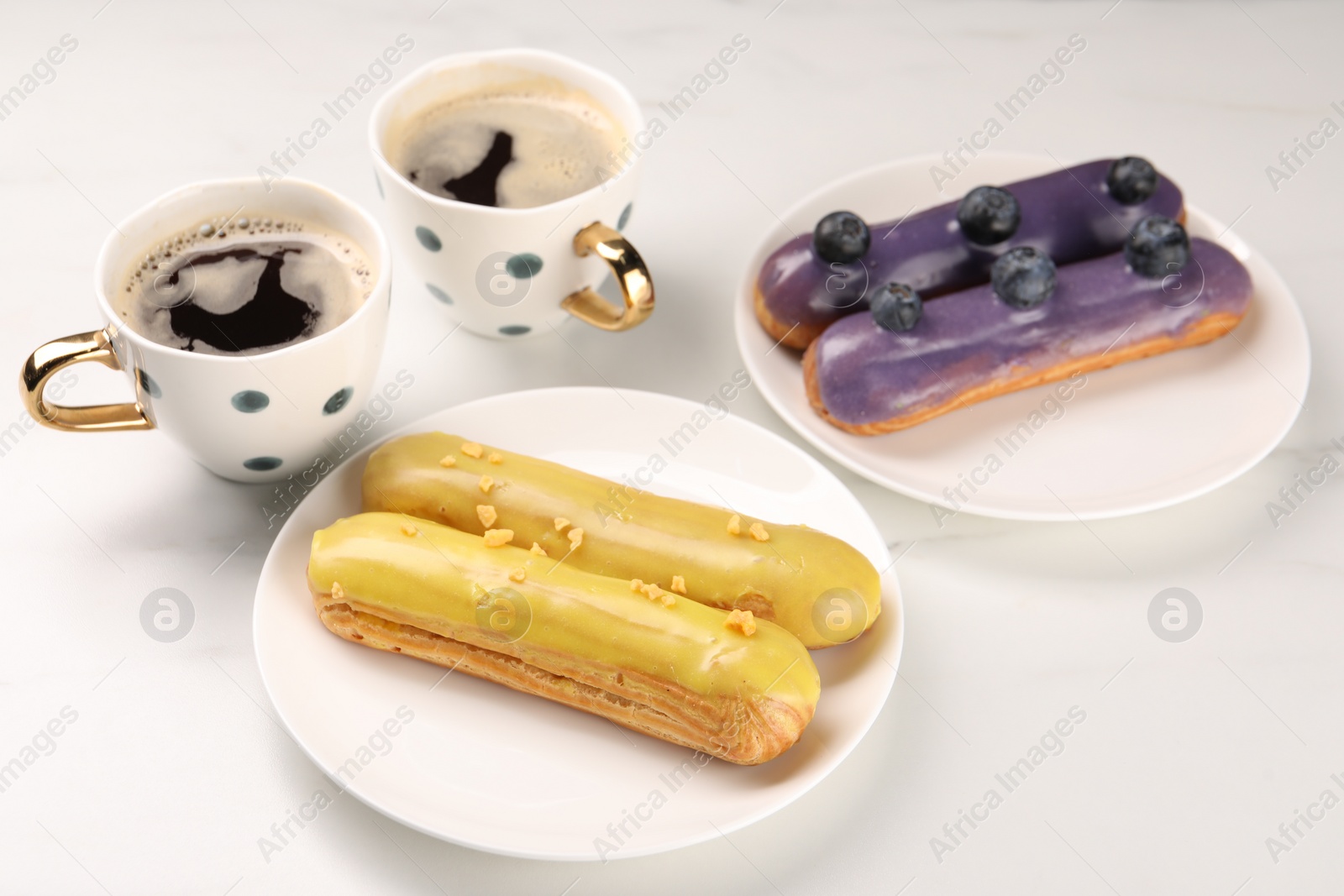 Photo of Tasty glazed eclairs and cups of coffee on white table, closeup