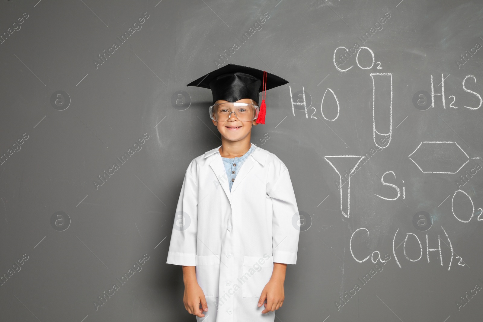 Photo of Little school child in laboratory uniform with graduate cap and chemical formulas on grey background