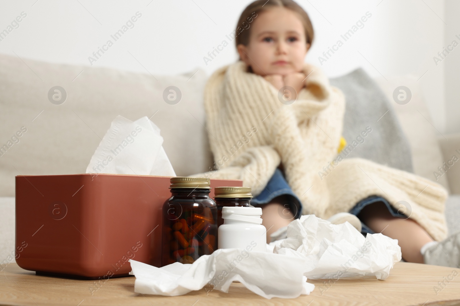 Photo of Girl with scarf around neck on sofa in room, focus on drugs. Cold symptoms