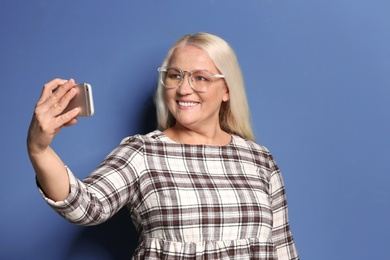 Photo of Beautiful mature woman taking selfie against color background