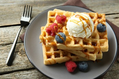 Delicious Belgian waffles with ice cream, berries and caramel sauce on wooden table, closeup