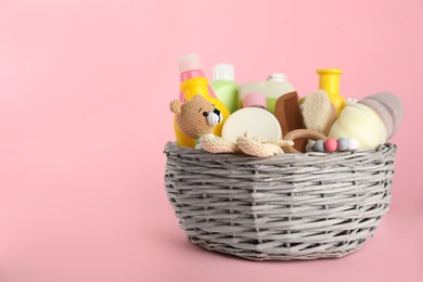 Wicker basket with baby cosmetics and accessories on pink background. Space for text