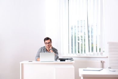 Handsome young man working with laptop at table in office