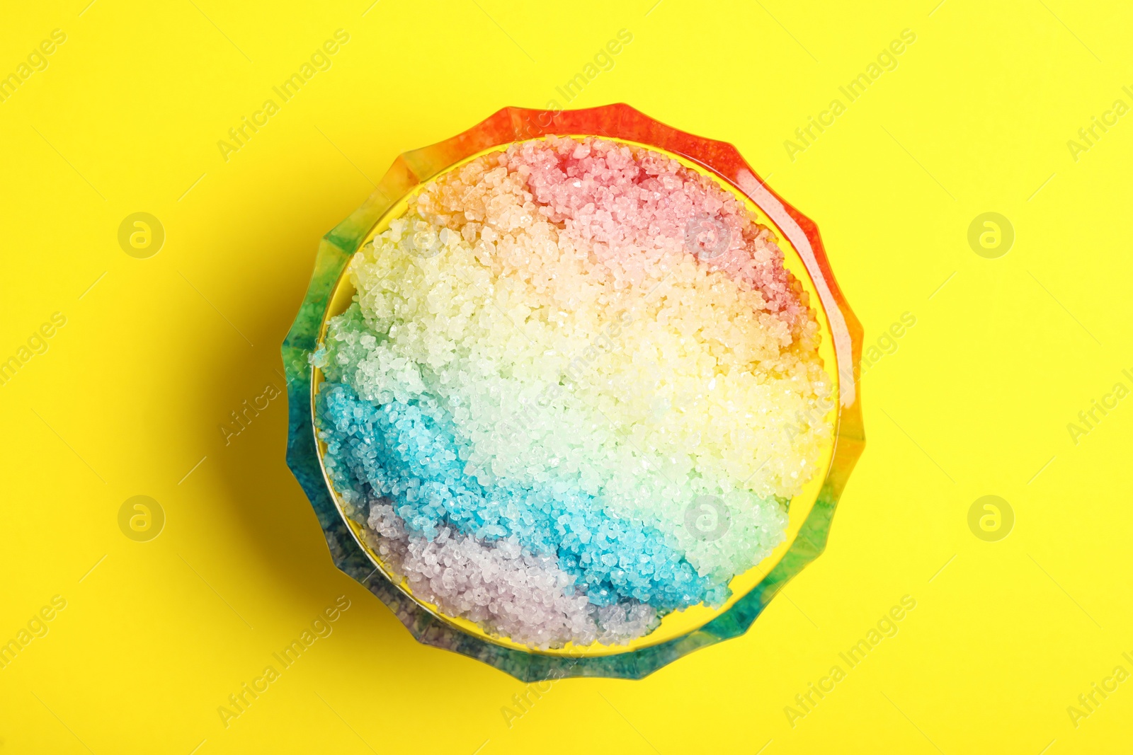 Photo of Rainbow shaving ice in glass dessert bowl on yellow background, top view