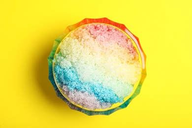 Photo of Rainbow shaving ice in glass dessert bowl on yellow background, top view