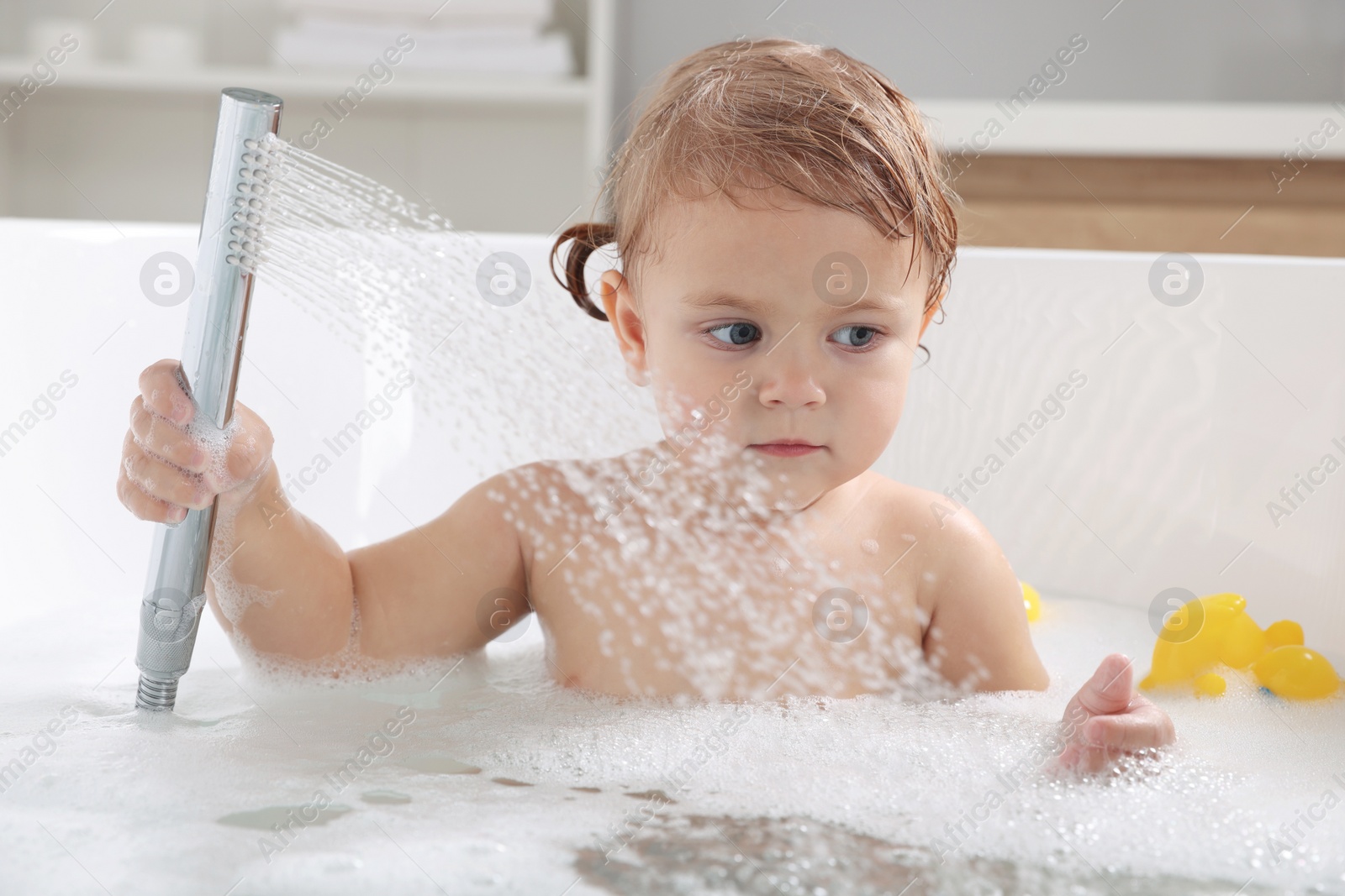 Photo of Cute little girl playing with shower head in bathtub at home