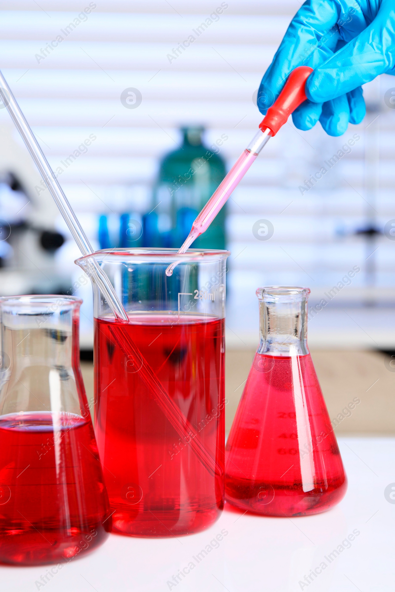 Photo of Laboratory analysis. Woman dripping red liquid into beaker on white table, closeup