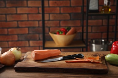 Photo of Carrot, peels, knife and other vegetables on wooden table in kitchen