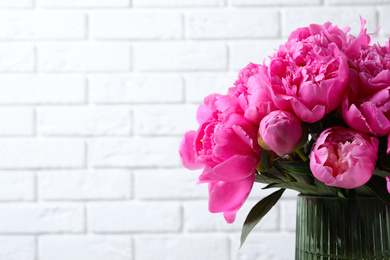 Photo of Bouquet of beautiful peonies in vase near white brick wall. Space for text