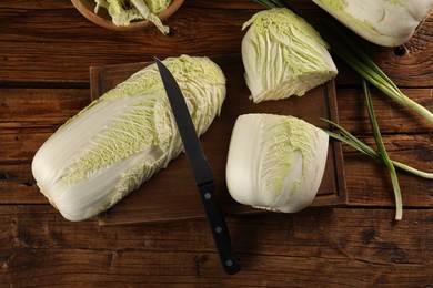 Photo of Fresh Chinese cabbages, green onion and knife on wooden table, flat lay