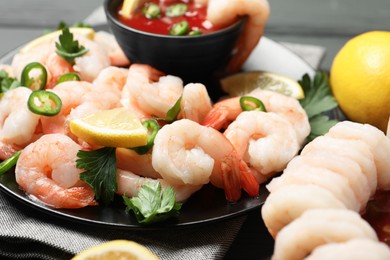 Photo of Tasty boiled shrimps with cocktail sauce, chili, parsley and lemon on table, closeup