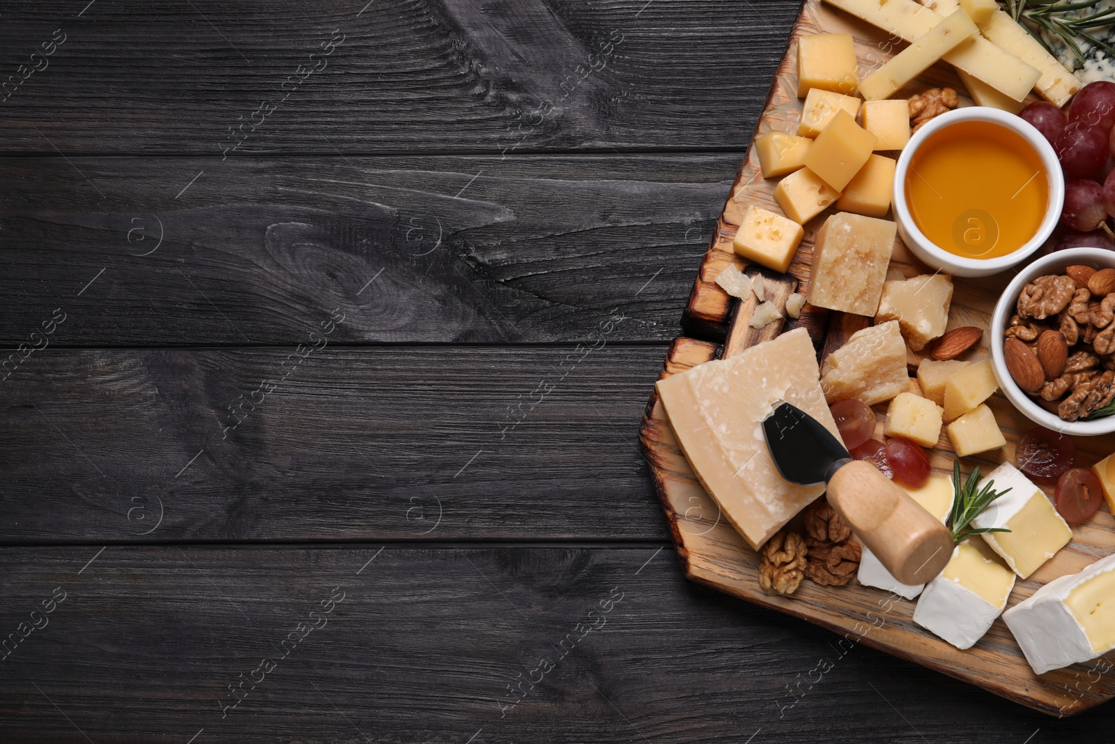 Photo of Cheese plate with honey, grapes and nuts on black wooden table, top view. Space for text