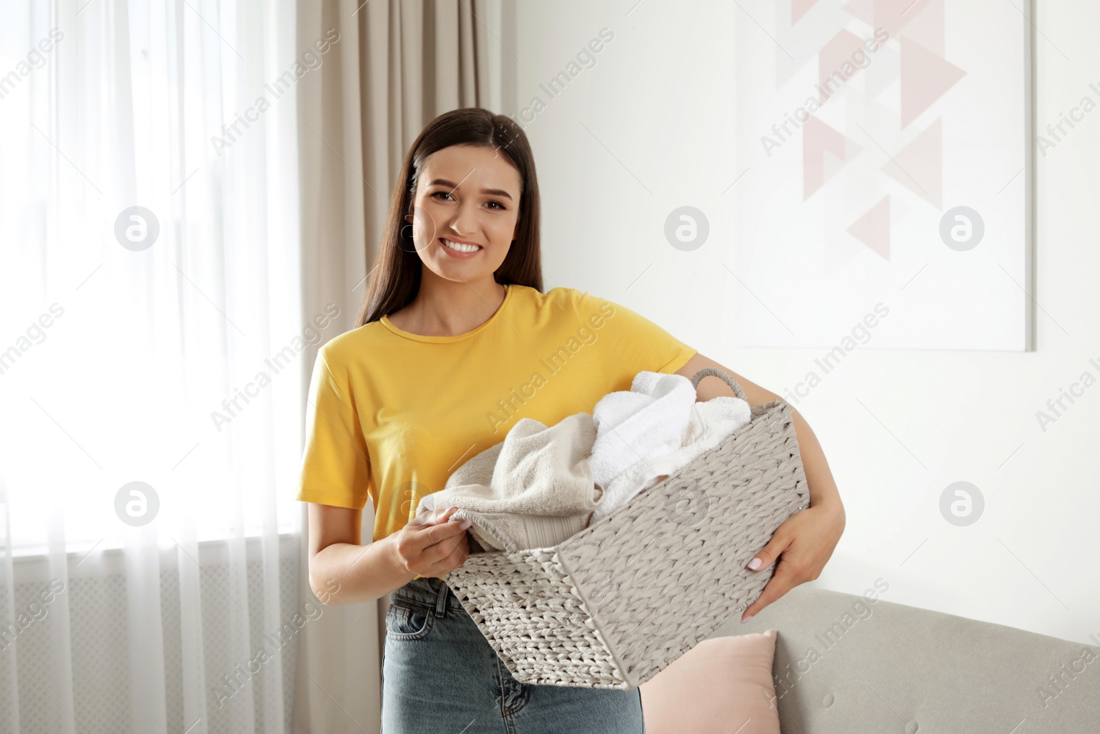 Photo of Young woman with laundry basket full of clean towels indoors