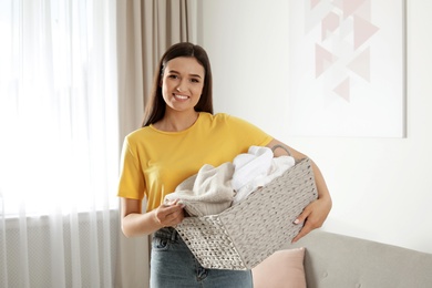 Photo of Young woman with laundry basket full of clean towels indoors