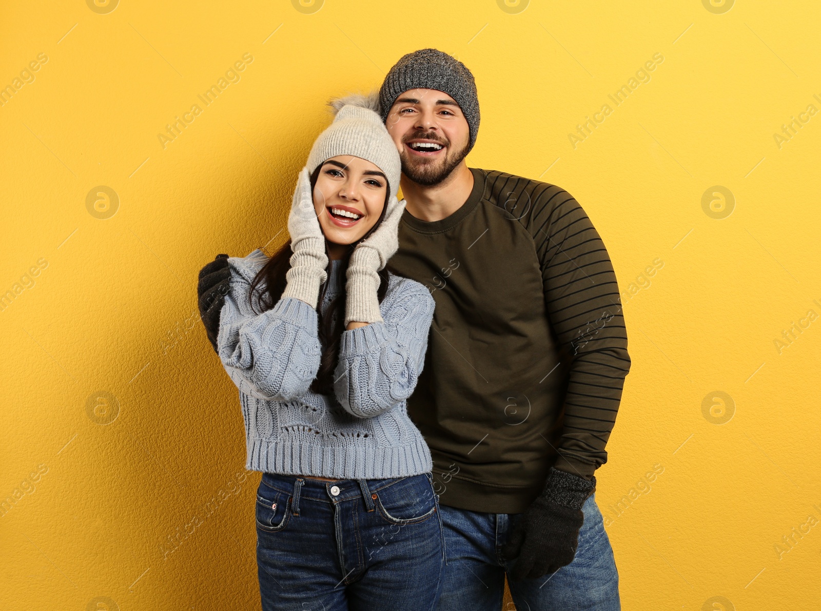 Photo of Happy young couple in warm clothes on yellow background. Winter vacation