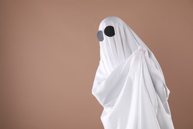 Photo of Creepy ghost. Person covered with white sheet on dark beige background, space for text