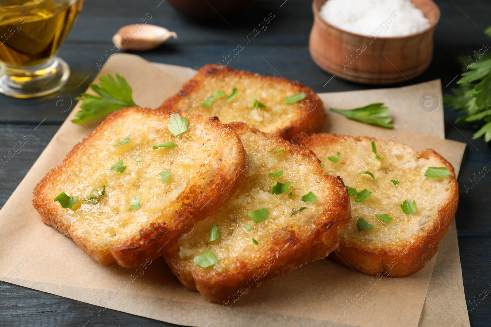 Photo of Slices of delicious toasted bread with garlic and herbs on blue wooden table, closeup