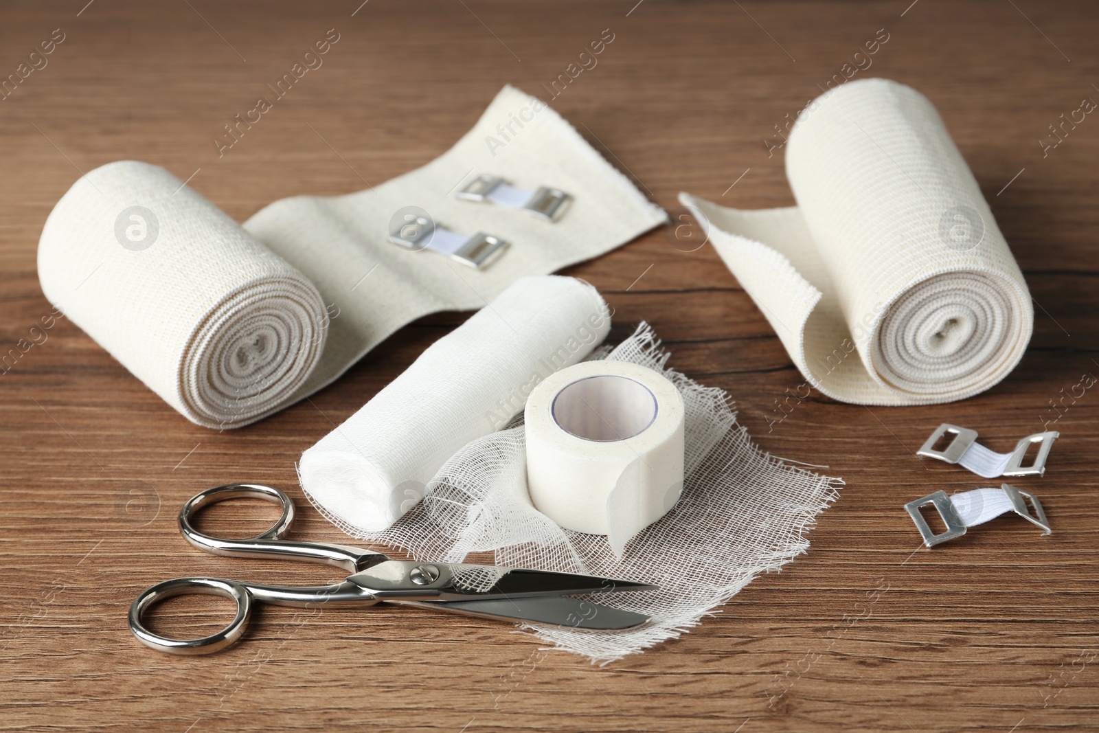 Photo of Medical bandage rolls, sticking plaster and scissors on wooden background