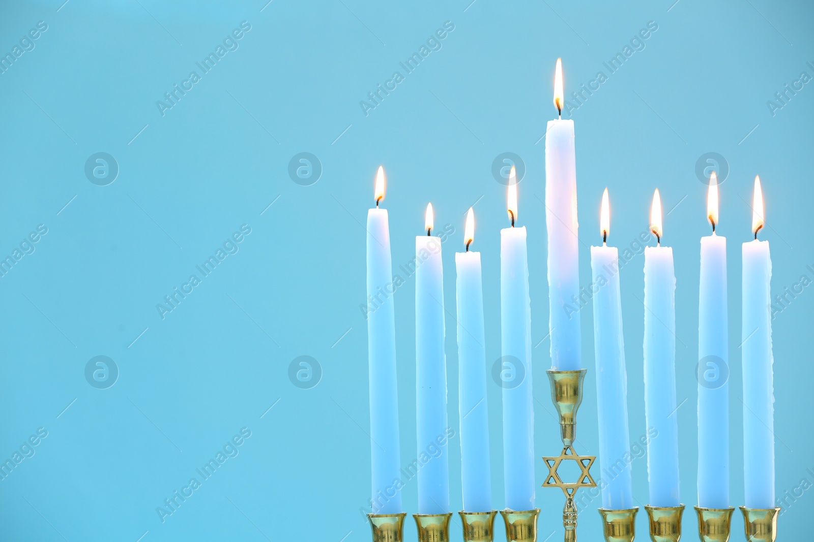 Photo of Hanukkah celebration. Menorah with burning candles on light blue background, closeup and space for text