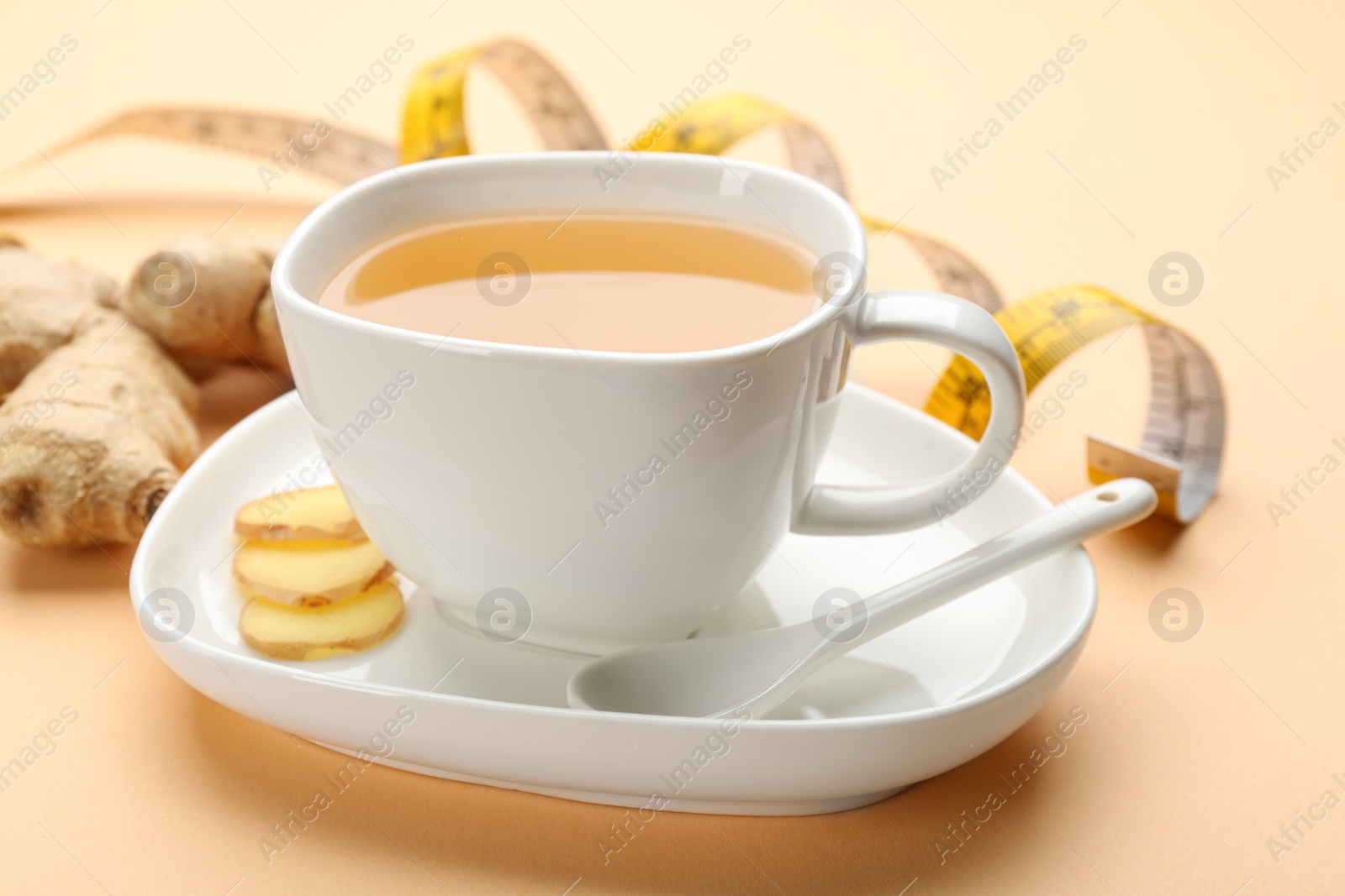 Photo of Cup of diet herbal tea and sliced ginger on orange background