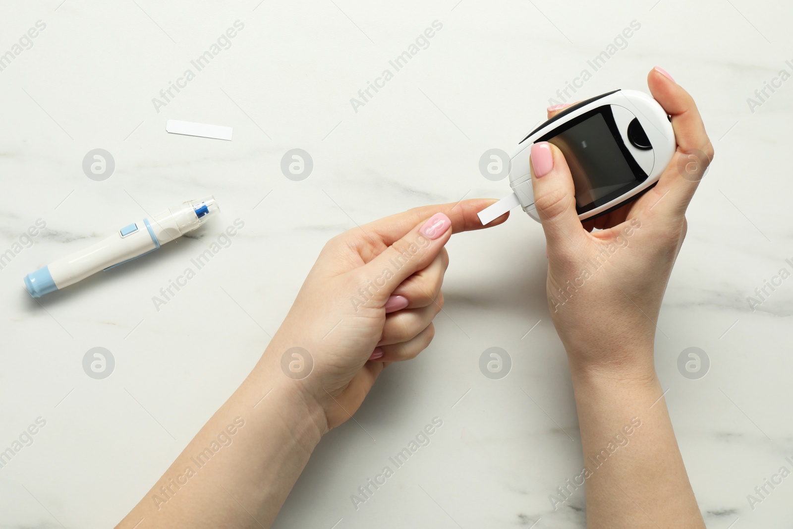 Photo of Diabetes. Woman checking blood sugar level with glucometer at white marble table, top view