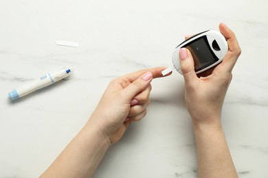 Diabetes. Woman checking blood sugar level with glucometer at white marble table, top view