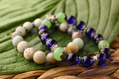 Photo of Beautiful bracelets with gemstones and green leaf on wicker surface, closeup